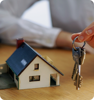 Hand holding house keys beside a model home