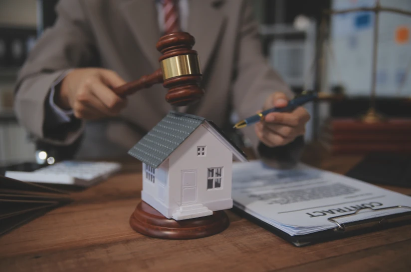Auctioneer's gavel beside a model house and a contract